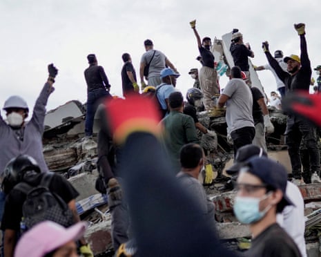 People raise their fists to call for silence to locate victims at the site of a collapsed building in Cali