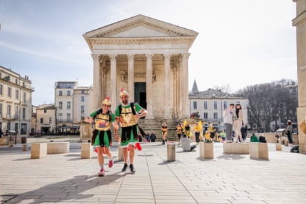 Two runners dressed as Roman soldiers stand in front of a Roman building in Nîmes