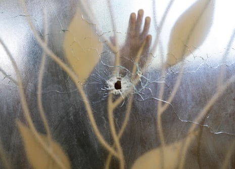 A hospital worker places his hand on a glass door pierced by a bullet hole