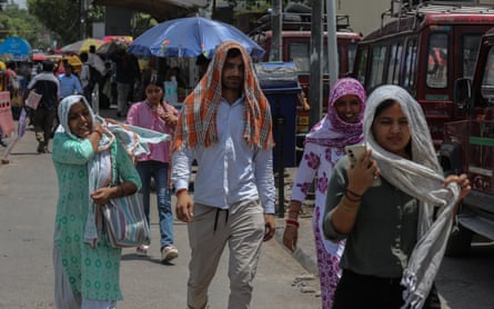 People walking on a street carrying umbrellas or wearing scarfs on their heads