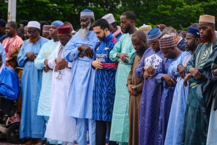 Zohran Mamdani in his Arsenal kurta standing and bowing his head with others during prayers outside