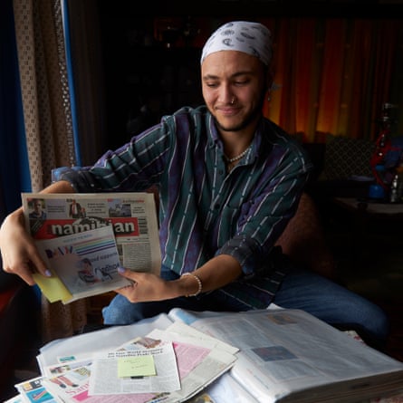 Omar van Reenen, wearing a bandana, holds up pages from newspapers from a selection spread on a small table