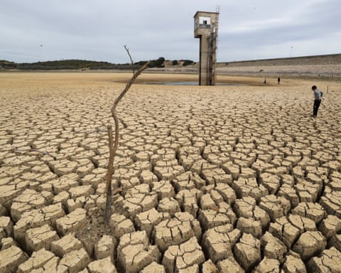 Solo seco e rachado na barragem de Chiba, em Nabeul, Tunísia, com uma pessoa e uma pequena torre ao fundo.