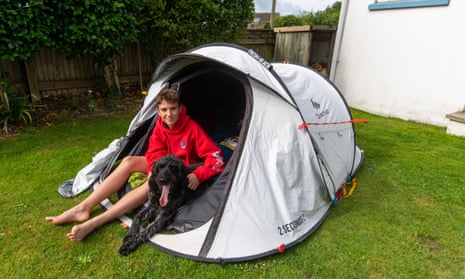 Max Woosey sits in his tent at home in Braunton, Devon, with Digby the labradoodle