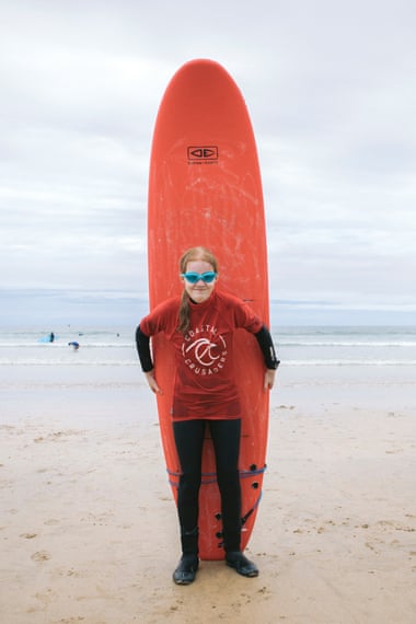 Hannah Rudlin-Jones stands in front of her red surfboard on the beach.