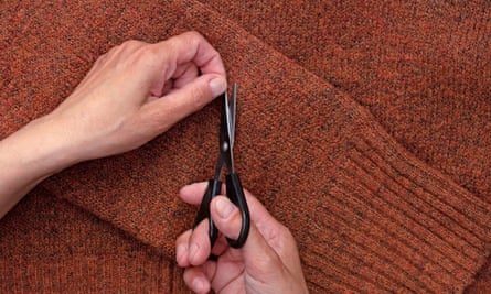 女人的手用剪刀从羊毛套头衫上剪下绒毛