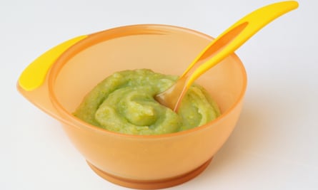 Above view of a baby bowl and spoon with pureed green food.