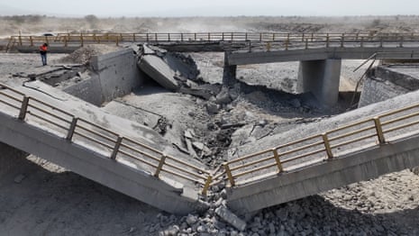 A damaged bridge lies in a riverbed, following US airstrikes.