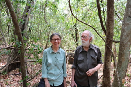 An older man and woman stand in a forest