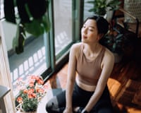 Active young Asian sports woman taking a break after working out at home, sitting on exercise mat taking a deep breath with her eyes closed. Sports and exercise routine. Health, fitness and wellness concept