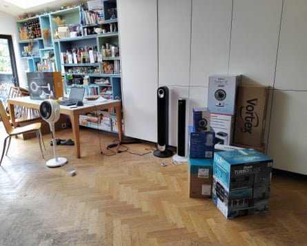 Several fans and boxes of fans in a home with a wooden floor, a desk and a full shelving unit