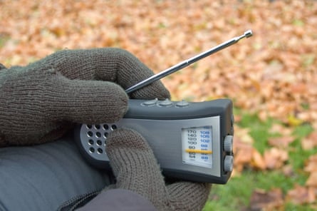 Gloved hands holding wind-up radio outdoor.