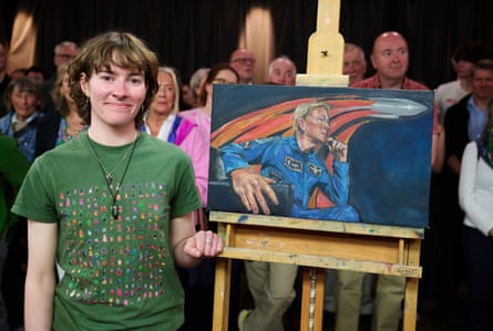 A young woman standing next to an easel with a portrait of Tim Peake with a rocket above his head