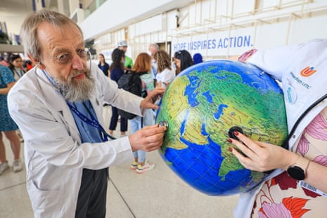 A man in a white jacket holding a stethoscope to a globe