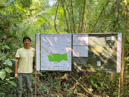 Raúl Bello Santa Cruz stands beside a map of the Kawsay Biological Station among vegetation