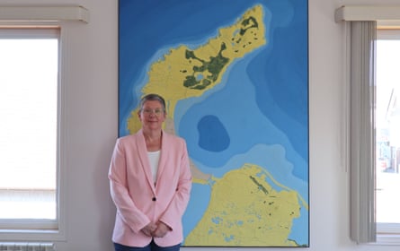 A middle-aged woman in a pink jacket stands in front of a map showing islands and the depth of the surrounding sea