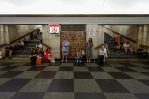 A crowd of people sat around and looking at their phones in a marble floored metro station in Kyiv