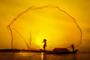 A fishermen tosses his net amid the sunset on the water in Vietnam