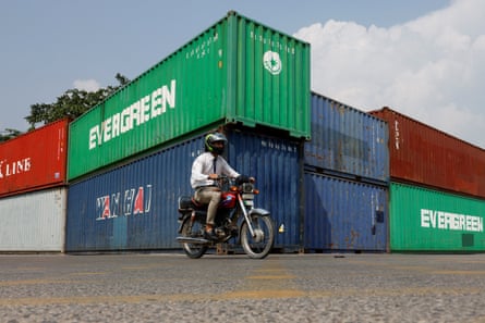 A man rides a motorbike past a stack of large red, green and blue shipping containers