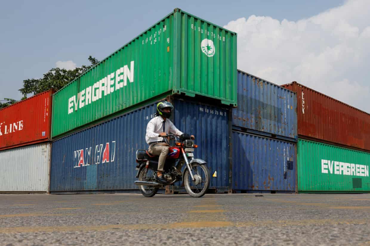 A man rides a motorbike past a stack of large red, green and blue shipping containers