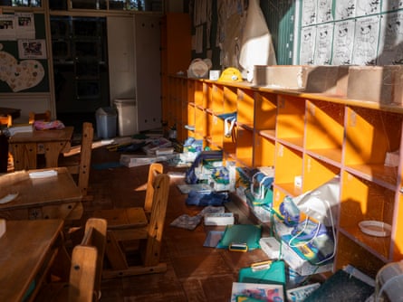 A school classroom with desks and shelving; bags and belongings are strewn on the floor