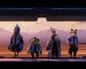 A still from the video game Star Fox. Its four anthropomorphic heroes (from left to right: a falcon, a toad, a hare and a fox) walk towards the camera, off a runway and into the large opening of a space craft, wearing white space jackets. There are mountains in the distance.