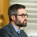 a man in a suit, tie and glasses looks ahead