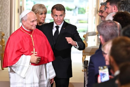 Macron walks the pope past a line of people inside building with exterior visible behind through doorway
