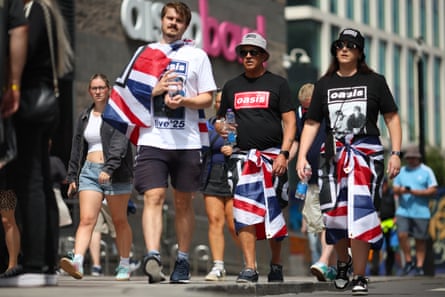 Fans wearing Oasis T-shirts and bucket hats walk down a street in Cardiff.