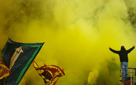 A fan stands among yellow flare smoke and flags during the Ligue 1 match between Lens and Marseille