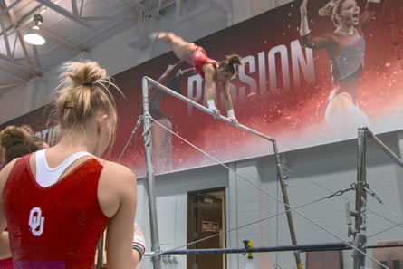 Maggie Nichols performs an uneven bars routine, swinging upside down, watched by a teammate