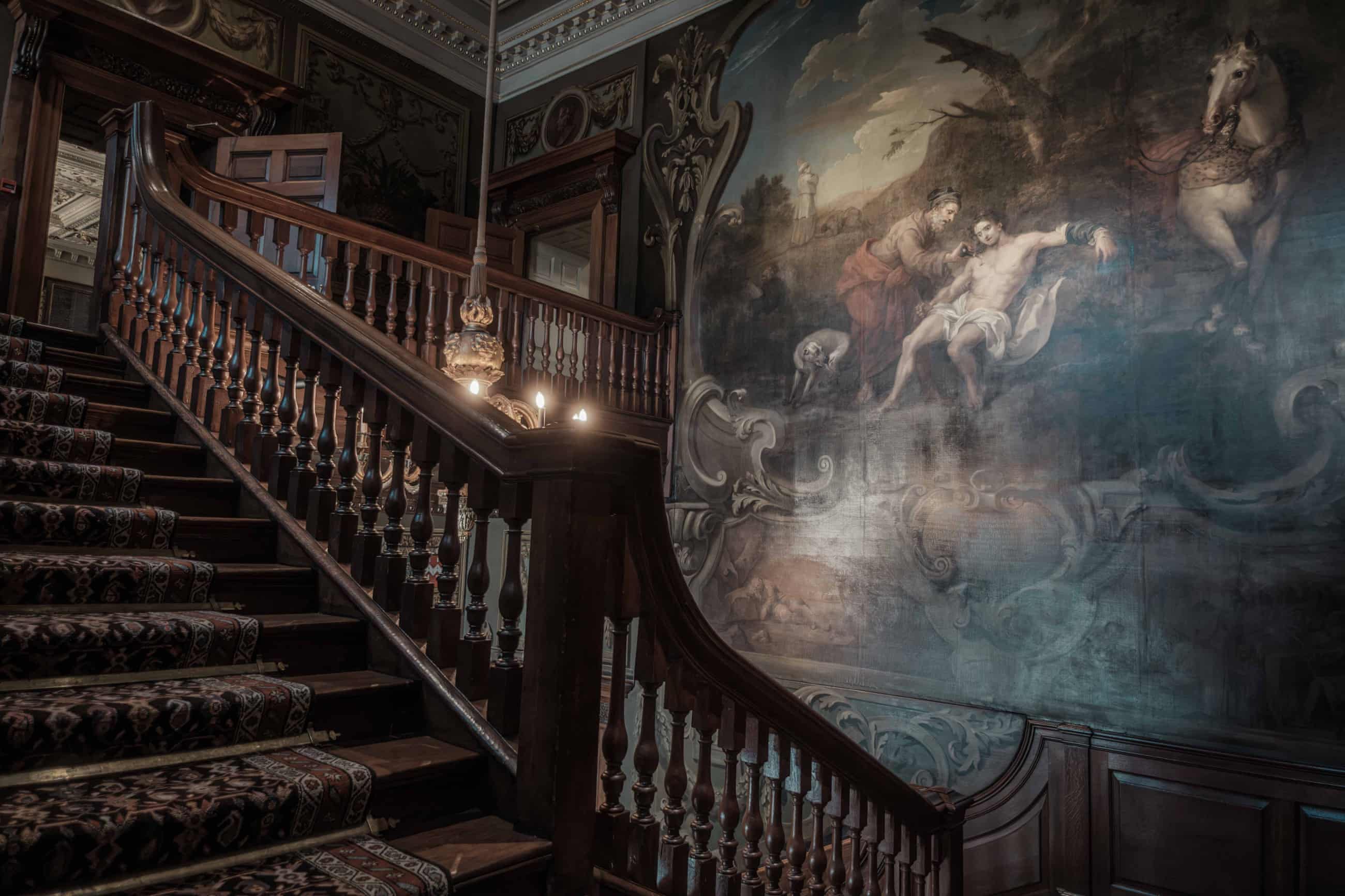 Grand, ornate staircase with a painting covering one wall