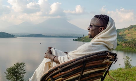 Makembe wears white robe while sitting overlooking lake and mountains