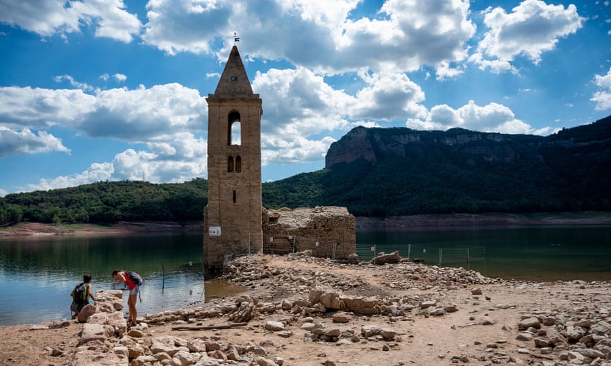 People stand in front of the ruins of the Church of Sant Roma de Sau. Normally, the bell tower is the only part of the church visible above water level.