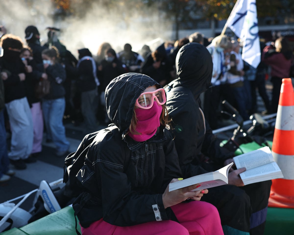 A protester reading a book reacts as tear gas sprayed by police is seen in the background during a blockade action part of a demonstration of high-school students near Helene Boucher high school in Paris.