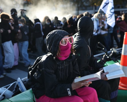 A protester reading a book as teargas is sprayed by police in the background