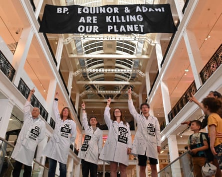 Five activists in white lab coats with ‘Coal out of our museums’ badges line up in the Science Museum’s energy hall under a banner that reads ‘BP, Equinor and Adani are killing our planet’