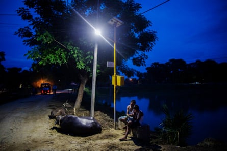 A man and child sit under a light powered from a solar microgrid at night in the village of Dharnai in Jehanabad