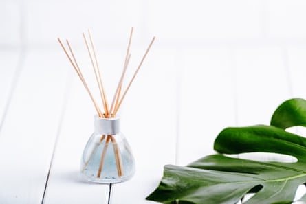 Reed fragrance diffusers in a jar on a white tiled surface with a monstera leaf on the side.