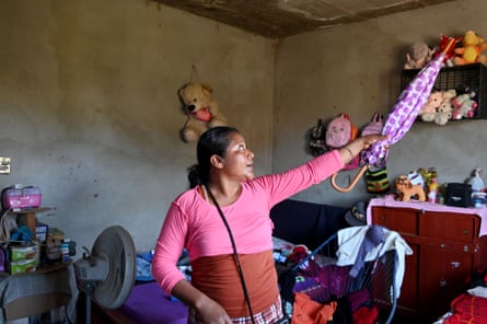 A woman standing in front of a bed in a room gestures with a closed umbrella