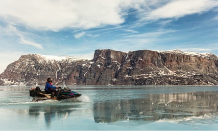 An Inuit hunter rides a skidoo through meltwater