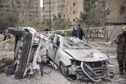 The twisted wreckage of two cars, one on its side, outside the apartment blocks
