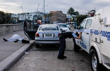 An overwhelmed police officer leans over a police vehicle near the bodies of Boris (69) and Sofia (61) Gurman