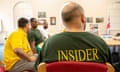 Man sitting with back to camera wearing green T.shirt saying 'Insider' in yellow capitals, at a table with several other men
