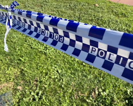 Blue and white checkered police tape stretches diagonally across green grass
