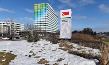 A sede da 3M: blocos de prédios brancos são vistos em um campo nevado contra um céu azul. Uma placa alta mostra o logotipo da empresa em letras vermelhas sobre fundo branco.