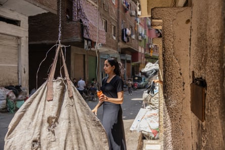 A woman wearing a black shift dress walks down a street with a large canvas bag full of rubbish in the foreground