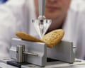A lab technician observes in the background as a machine with a pointed instrument breaks a biscuit in half
