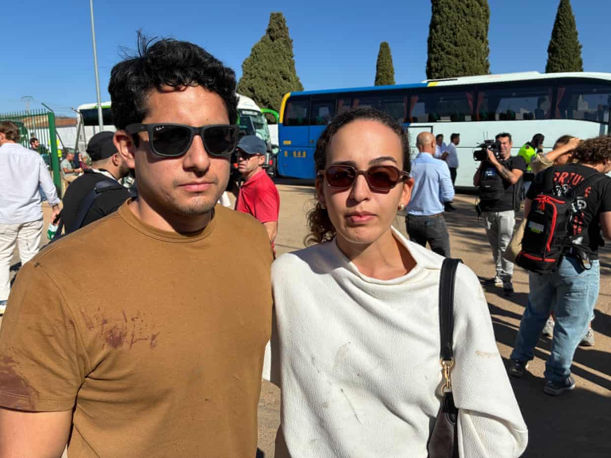 Josimar Medina, wearing sunglasses and a brown T-shirt stained with the blood of a passenger he'd helped tend to after the accident, and his girlfriend, Vitoria Maia, who is wearing a sunglasses, a white top and a dark handbag across her left shoulder