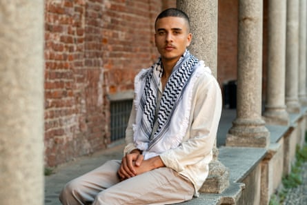 A man wearing a keffiyeh scarf sits in a colonnade